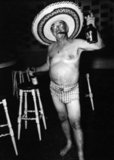 Constantino Arias' photo shows an American tourist in 1950's Batista-era Havana, Cuba. The man is wearing a bathing suit and sombrero, holding a liquor bottle in each hand. This photo featured as part of the 2010 exhibit 'Cuba in Revolution', at the International Center of Photography in New York City, USA.
